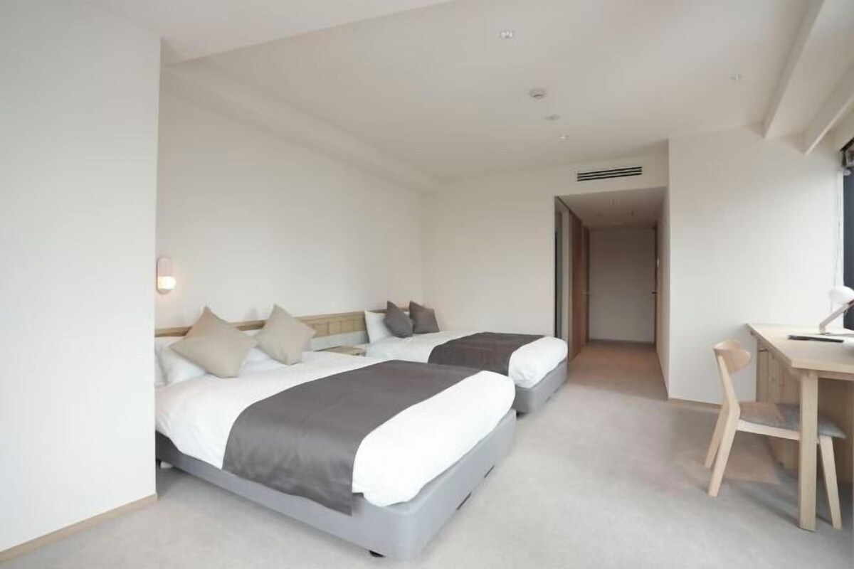 A modern hotel room with two beds, a desk, and a chair.