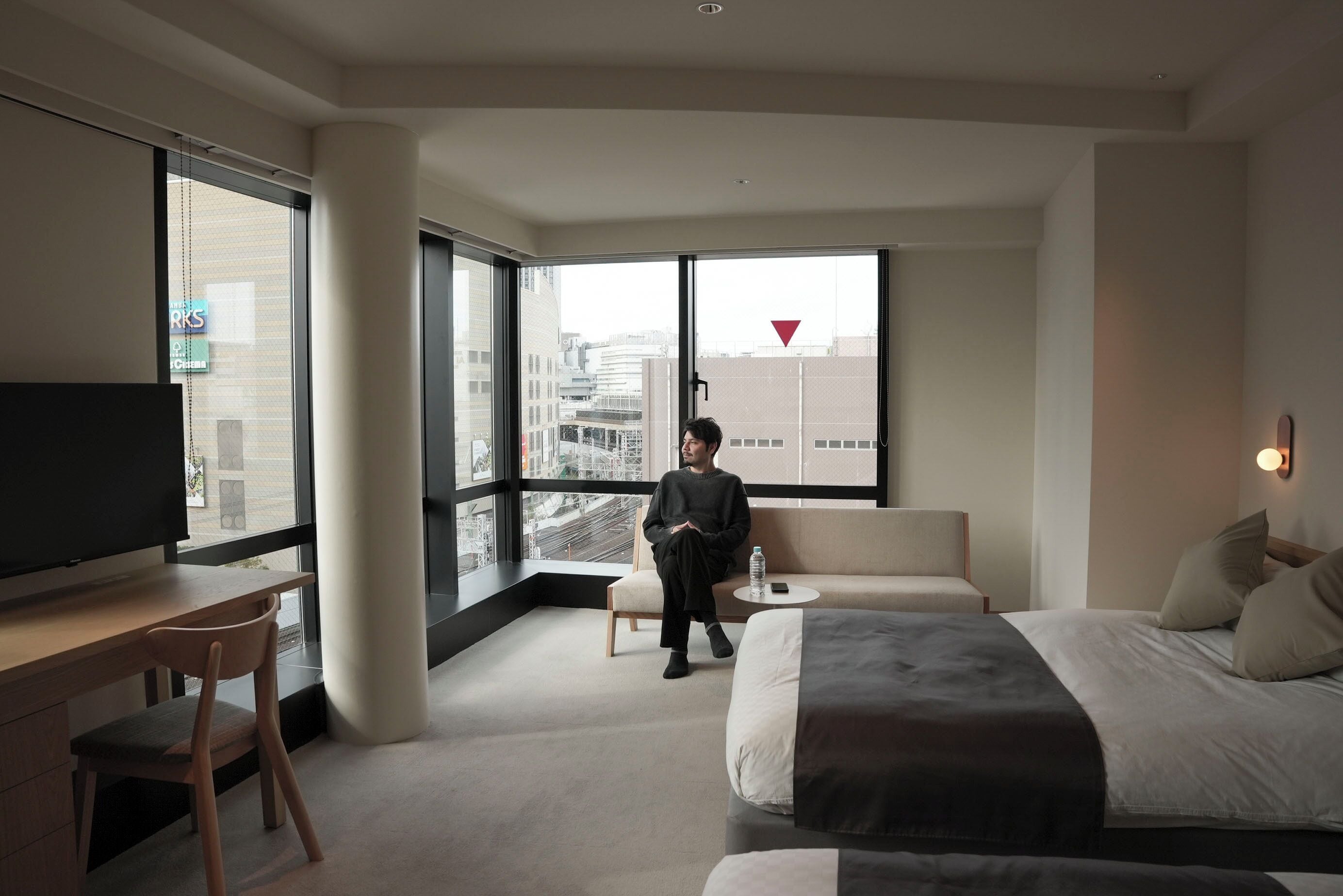 A modern hotel room with a large bed, a desk, a chair, and a sofa.