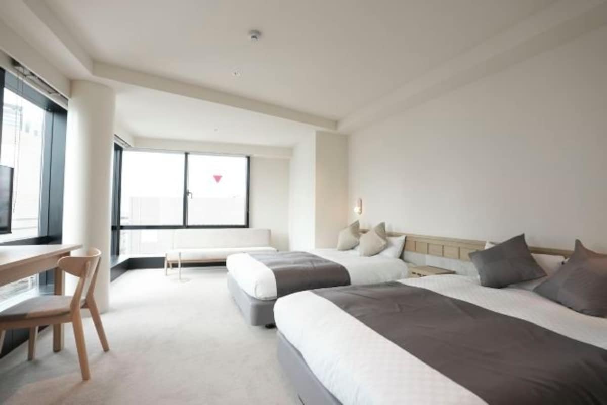 Habitación de hotel con dos camas, un escritorio y un ventanal amplio.