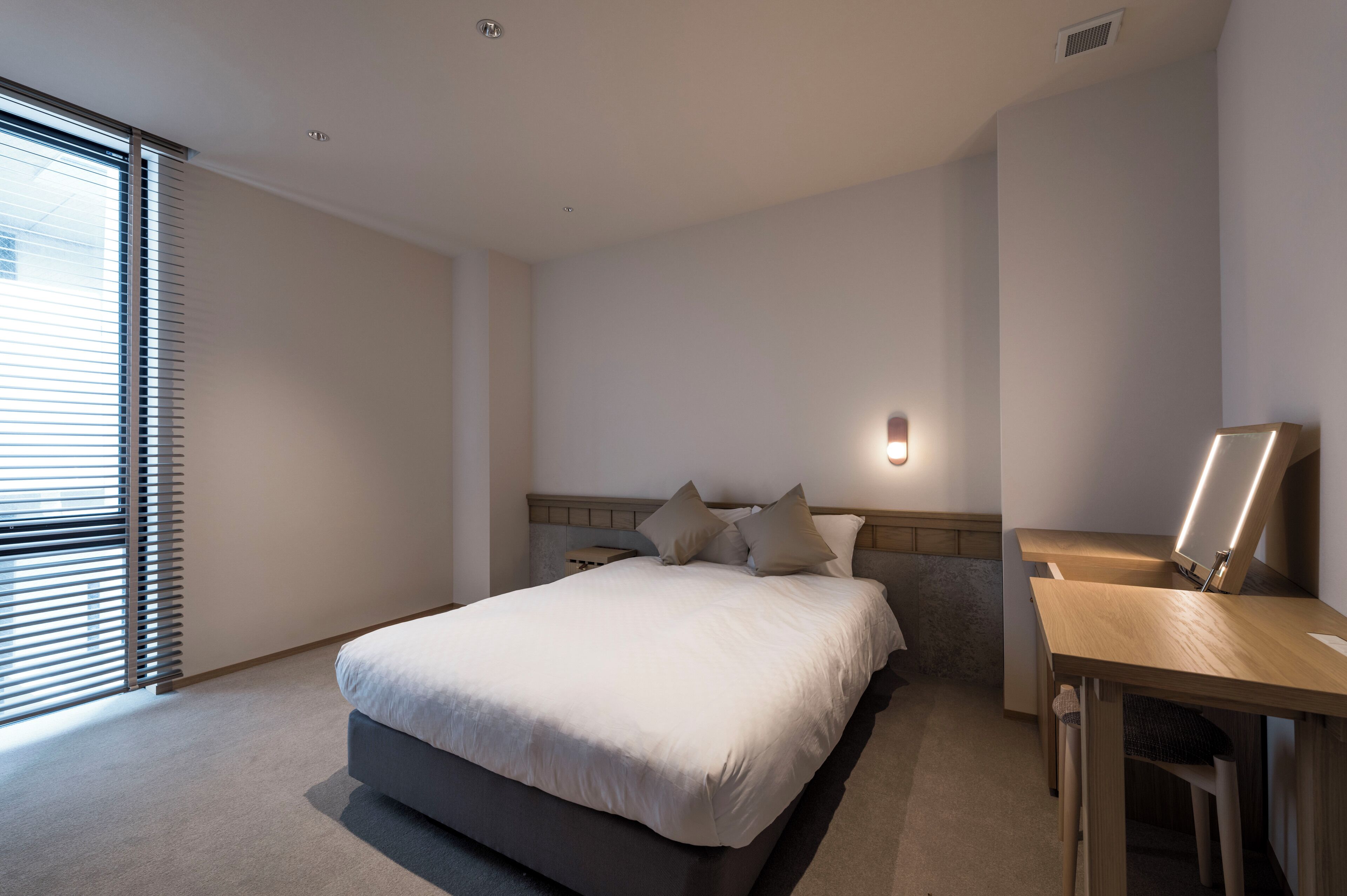 A modern bedroom with a bed, bedside table, and a desk with a lamp.
