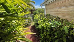 Un sendero de jardín que lleva a un edificio con una cerca blanca decorativa y un muro de bambú.