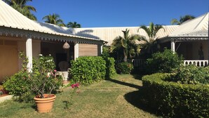 Una cabaña con un porche cubierto, un pequeño jardín con plantas en macetas y un cielo azul despejado.