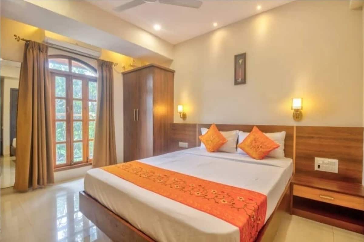 A hotel room with a bed, nightstands, a wardrobe, and a window with curtains.