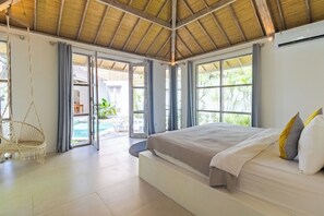 A spacious bedroom with a large bed, a hanging chair, and a view of an outdoor swimming pool. - Villa Cocodrilos 1 by Pertama Stay (Seminyak)