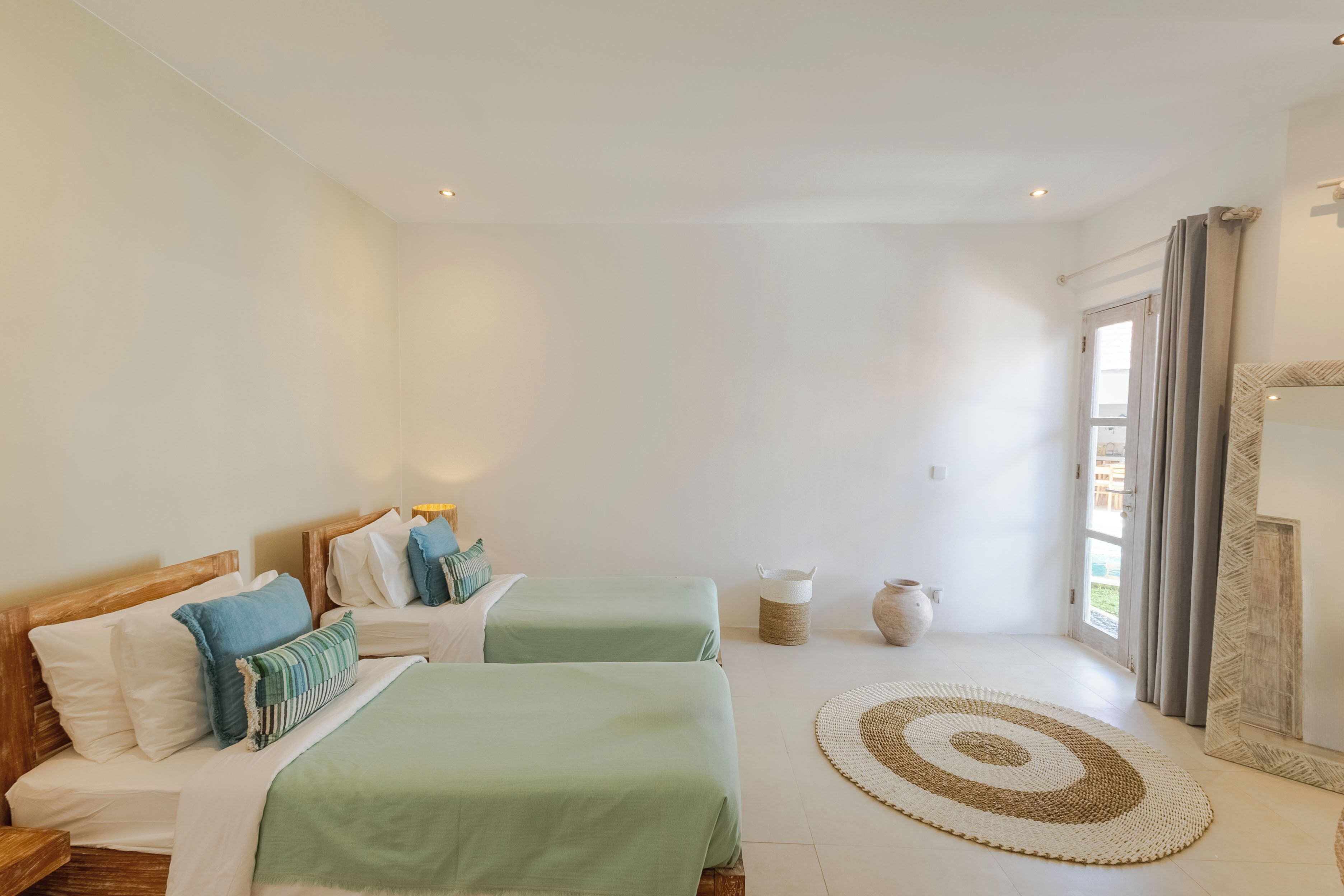 Une chambre avec deux lits, une grande fenêtre et un tapis rond.