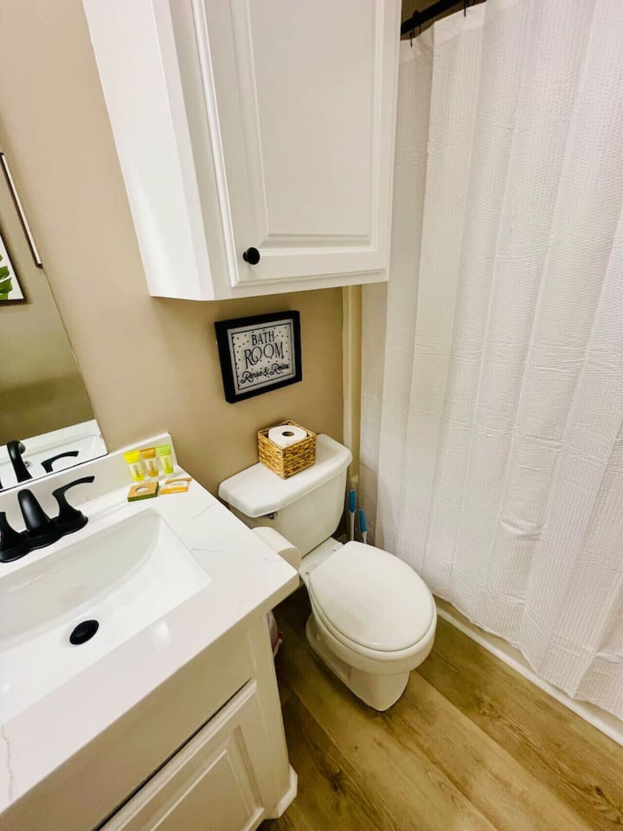 Un baño con lavamanos blanco, inodoro y un cartel enmarcado sobre el inodoro que dice 'BATHROOM'.