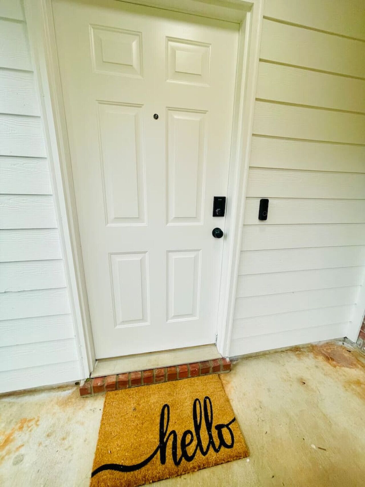 A white door with a doormat that reads "hello" and a small black device on the wall to the right.