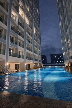 A swimming pool with a view of high-rise buildings at dusk. - L.CONDOTEL | Private Suite w/ Balcony, TV & Fridge – Near MOA & Airport (Parañaque)