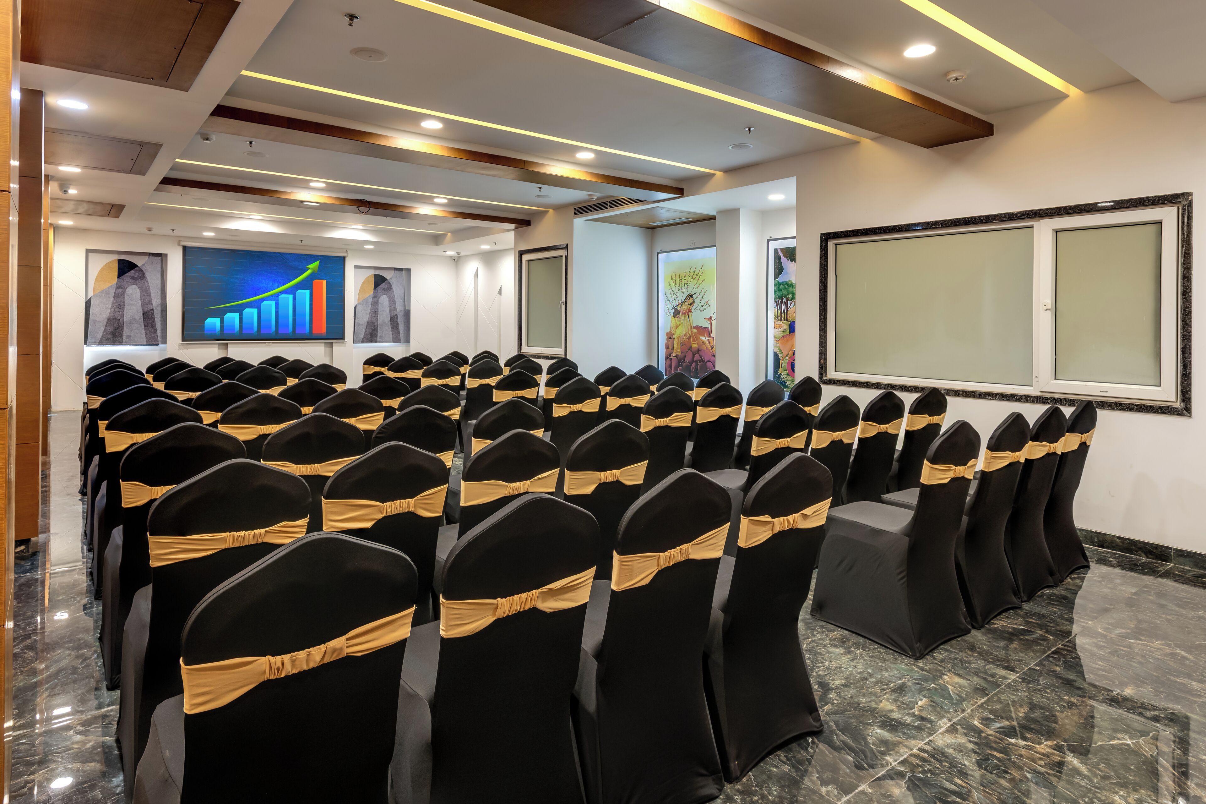 A conference room with rows of chairs, a large screen, and artwork on the walls.