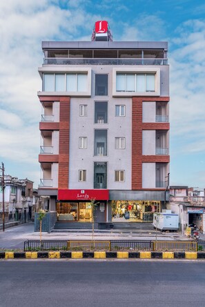 A multi-story hotel with a red and grey facade, a visible restaurant at the ground level, and a clear sky in the background.