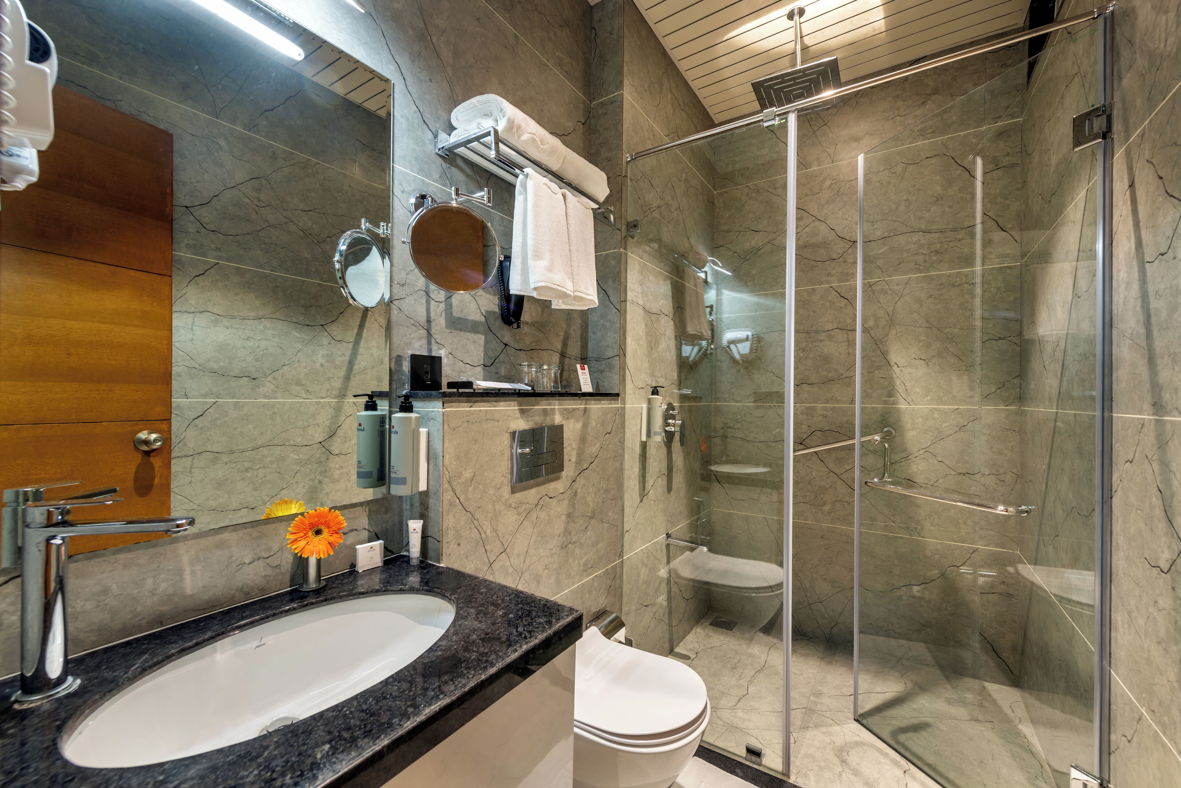 A modern bathroom with a marble sink, a glass shower enclosure, and a wooden vanity.