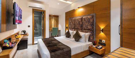A modern hotel room with a large bed, a desk with a computer, a TV, and a minibar.