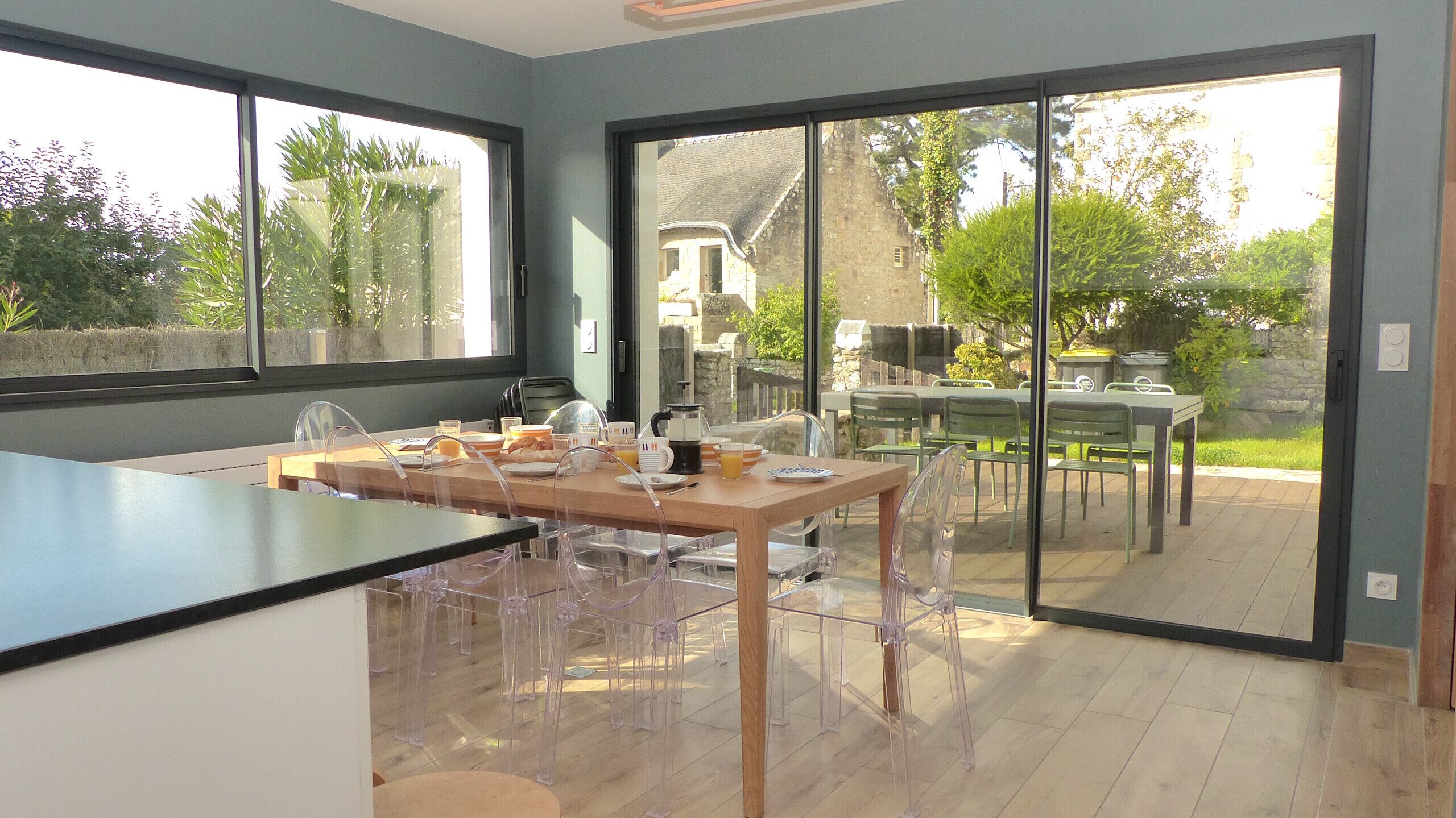 Cocina moderna con una isla grande, comedor con sillas y vistas al jardín a través de puertas de vidrio.