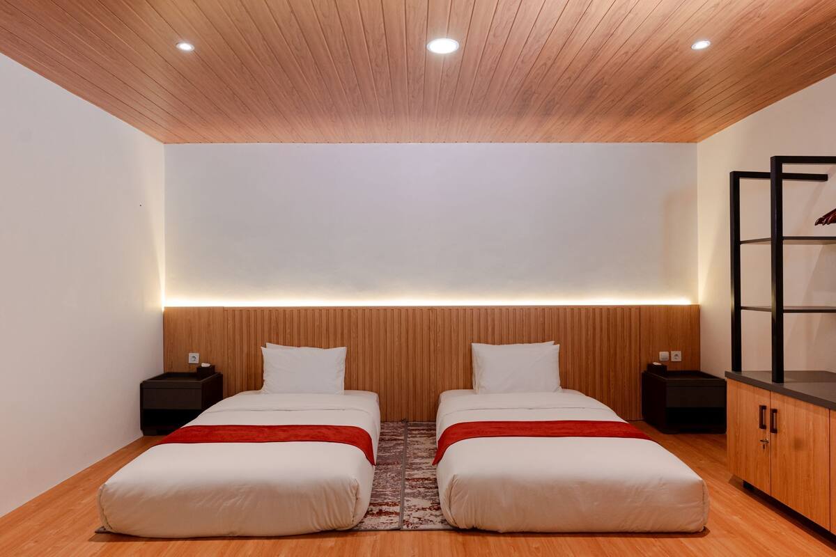 A modern bedroom with two beds, wooden paneling on the ceiling, and a built-in shelf unit.