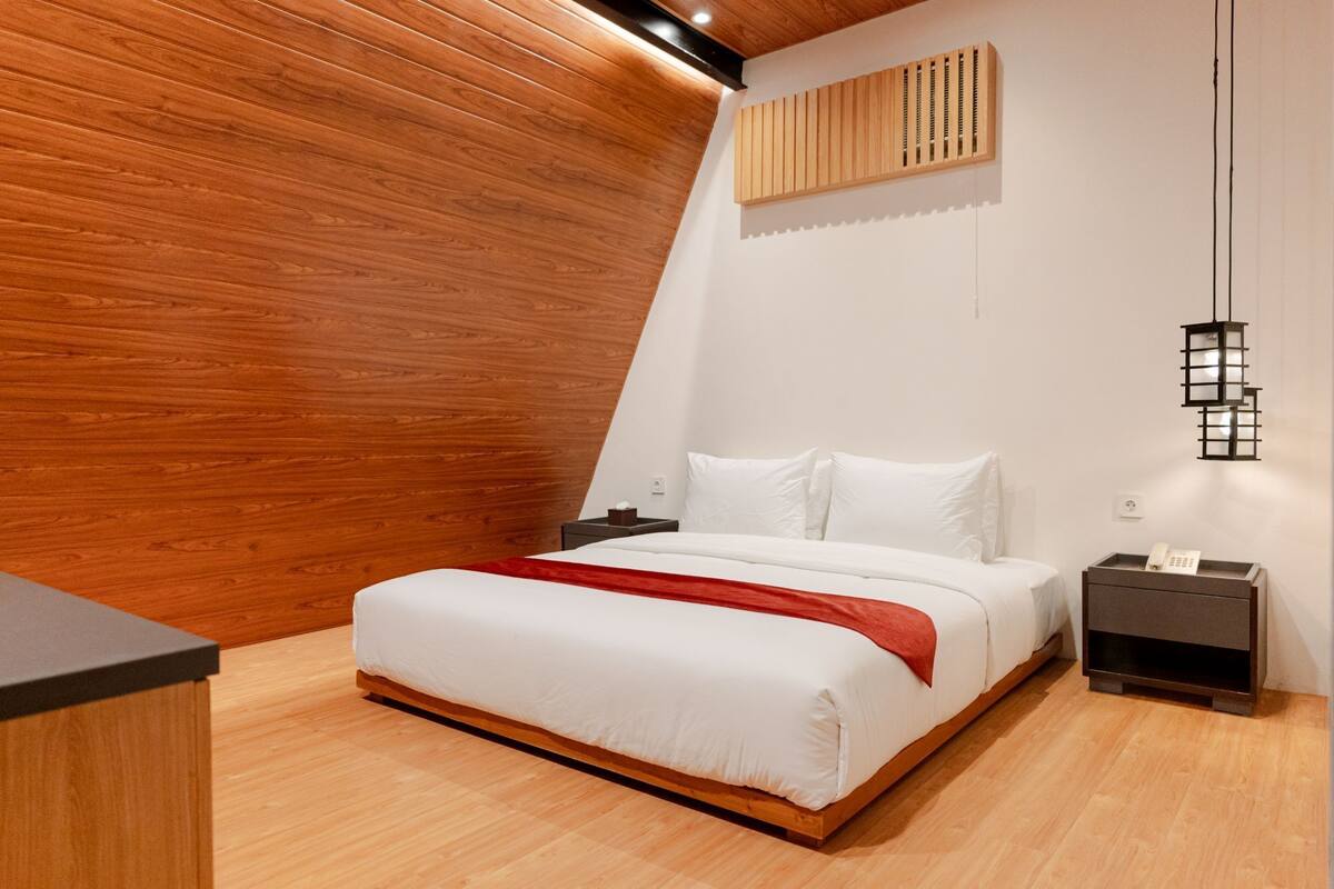 A modern bedroom with a sloped ceiling, wooden paneling, a large bed with white bedding, two bedside tables, and a hanging light fixture.