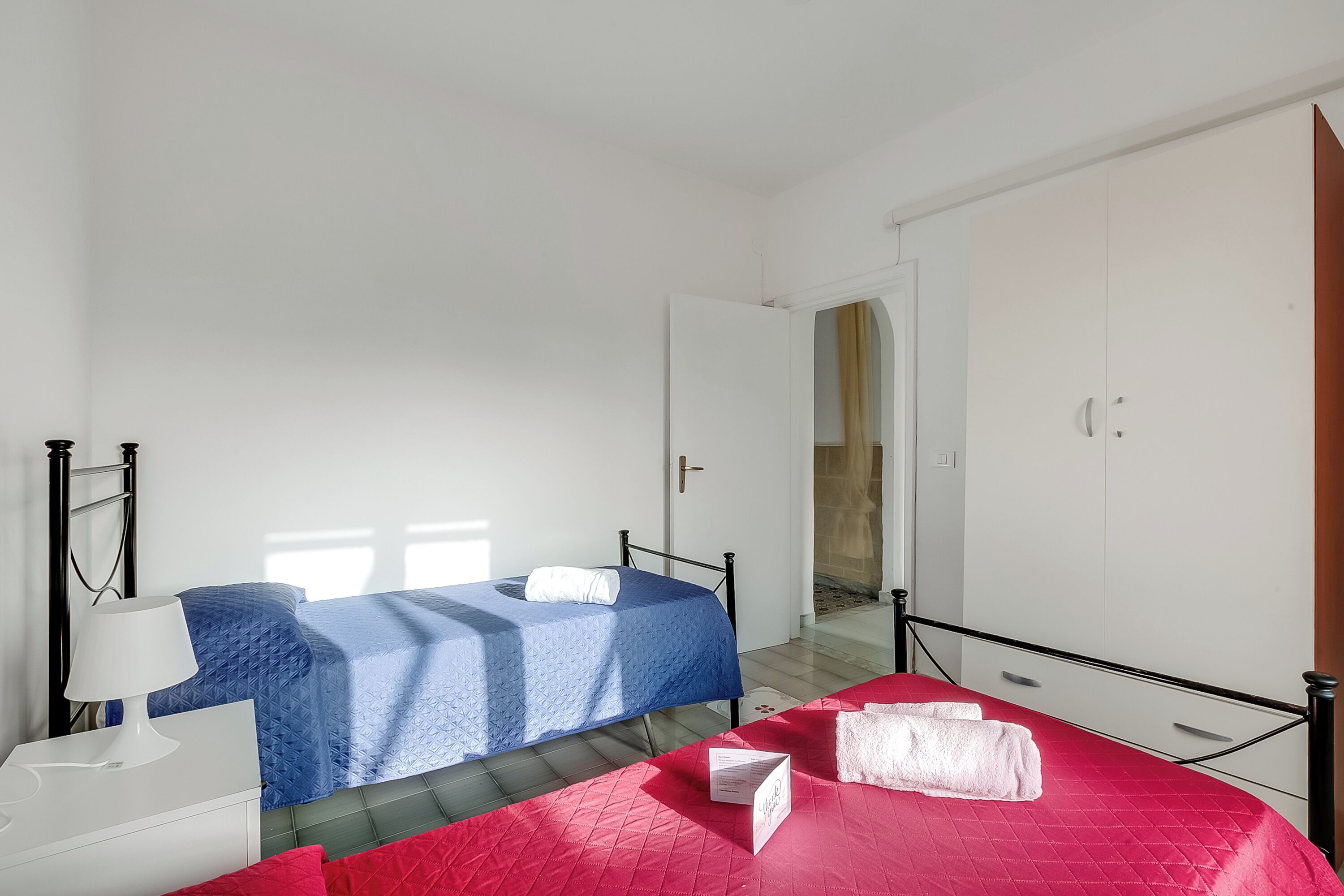 Una camera da letto con due letti, un comodino bianco, una coperta rossa e una parete bianca.