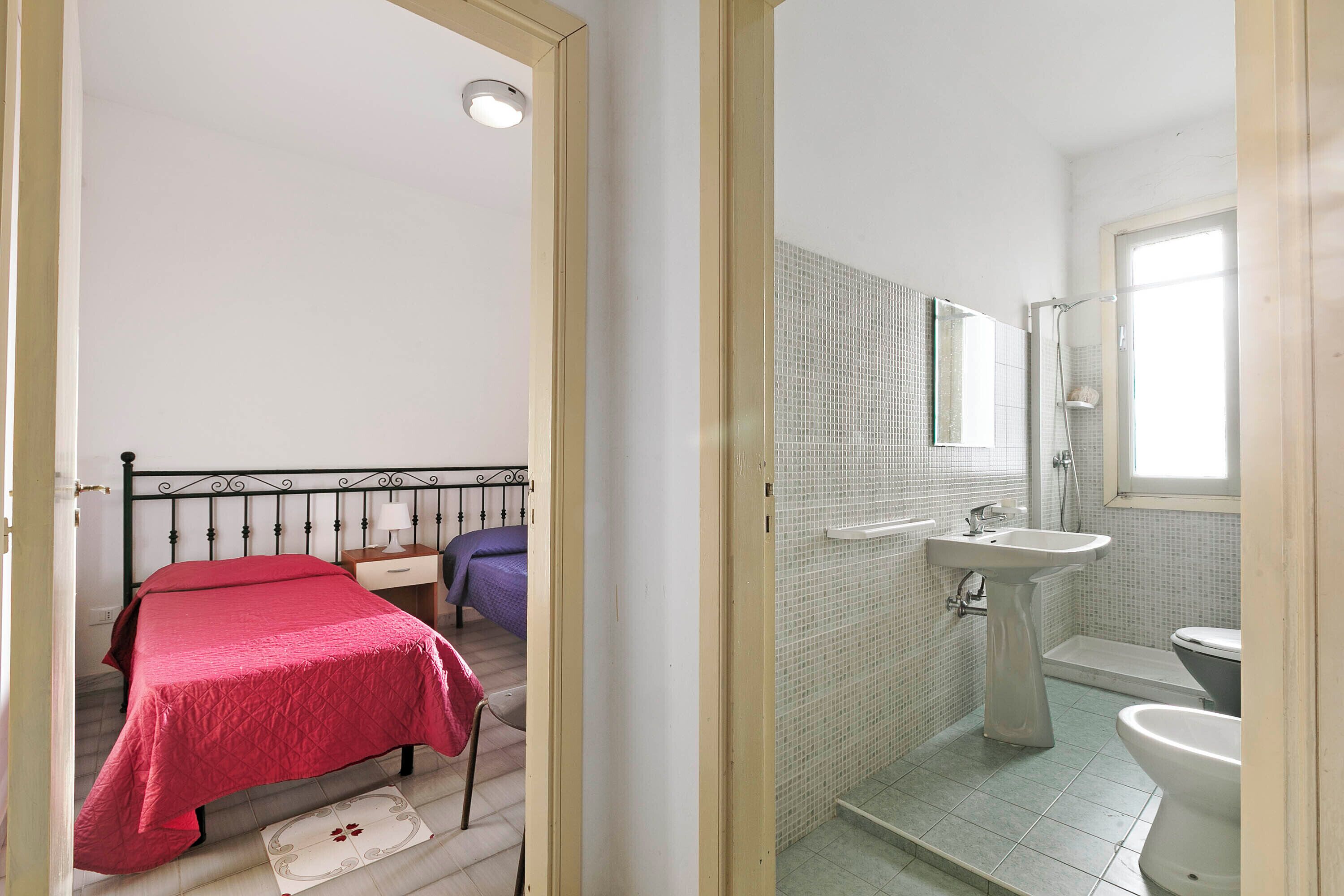 Ein Schlafzimmer mit Bett und Nachttisch, ein Badezimmer mit Waschbecken und Toilette sowie ein Fenster, das natürliches Licht hereinlässt.