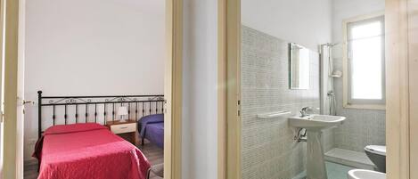 Ein Schlafzimmer mit Bett und Nachttisch, ein Badezimmer mit Waschbecken und Toilette sowie ein Fenster, das natürliches Licht hereinlässt.