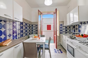 Una cocina con armarios blancos, una mesa de comedor con sillas, una estufa y un refrigerador.