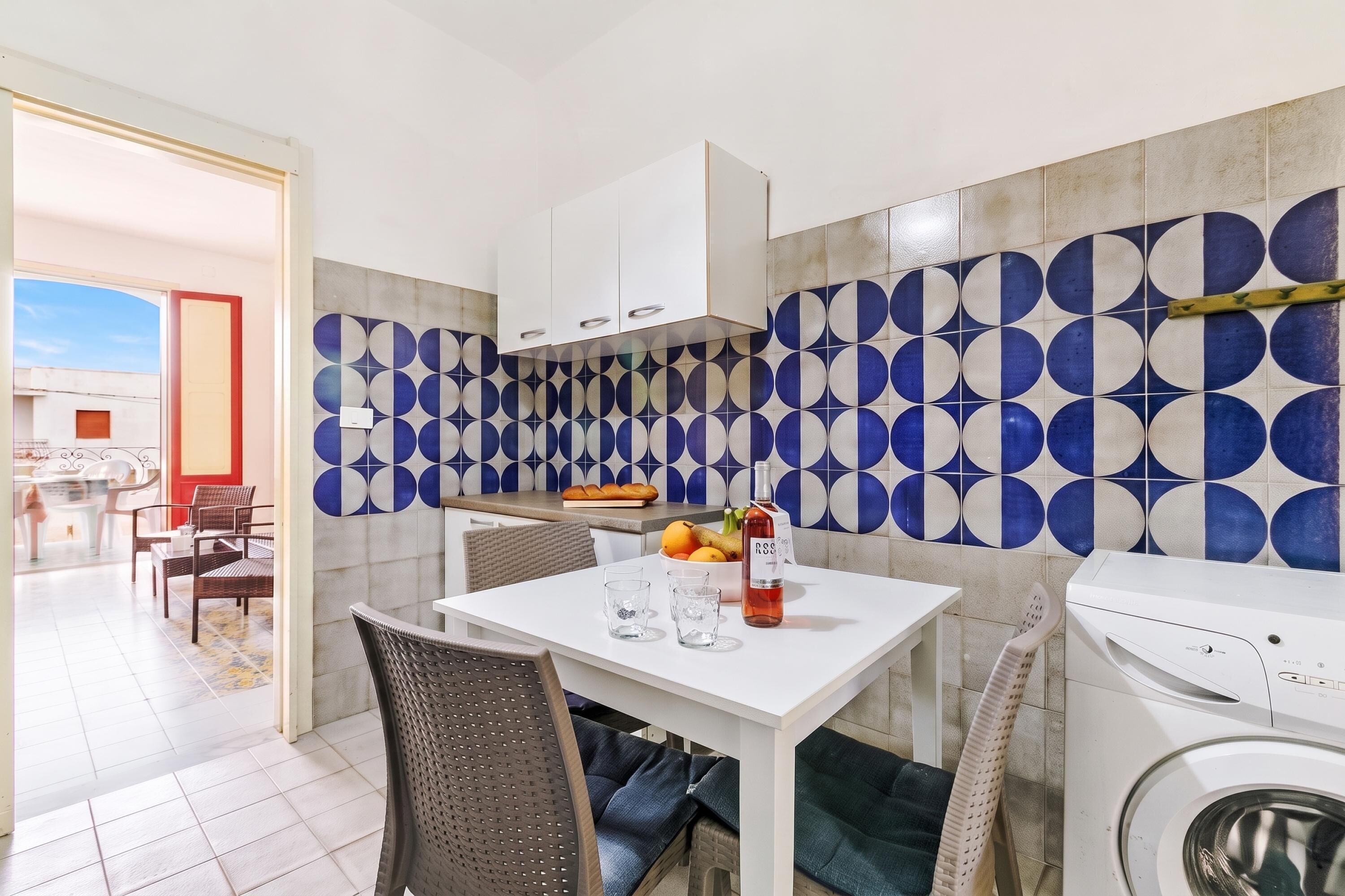 Une cuisine moderne avec un revêtement mural en carreaux aux motifs géométriques, un coin repas avec une table et des chaises, et un lave-linge.