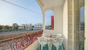 Un balcon avec une table dressée pour le dîner, des chaises blanches et une rambarde rouge.