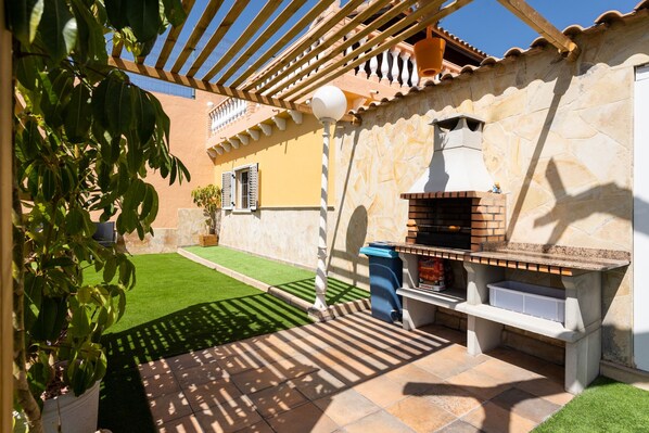 An outdoor patio with a brick oven, a pergola, and a small garden area.