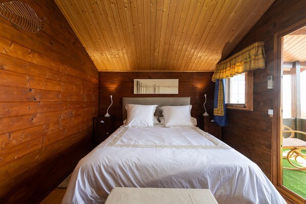 Un dormitorio de cabaña de madera con una cama, mesitas de noche y una ventana con cortinas.