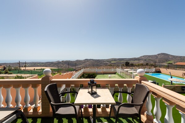 Un balcón con dos sillas y una mesa, con vistas a una piscina y un paisaje montañoso.