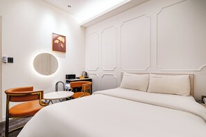 A hotel room with a bed, two chairs, a small table, a mirror, and a wall-mounted artwork.