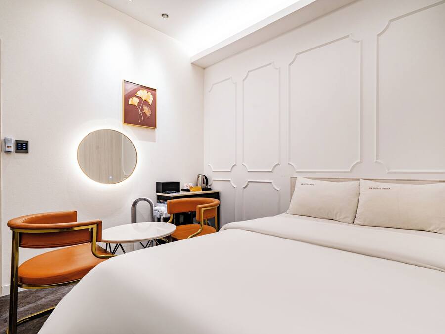 Habitación de hotel con una cama, dos sillas, una mesita, un espejo y una obra de arte colgada en la pared.