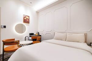 Habitación de hotel con una cama, dos sillas, una mesita, un espejo y una obra de arte colgada en la pared.