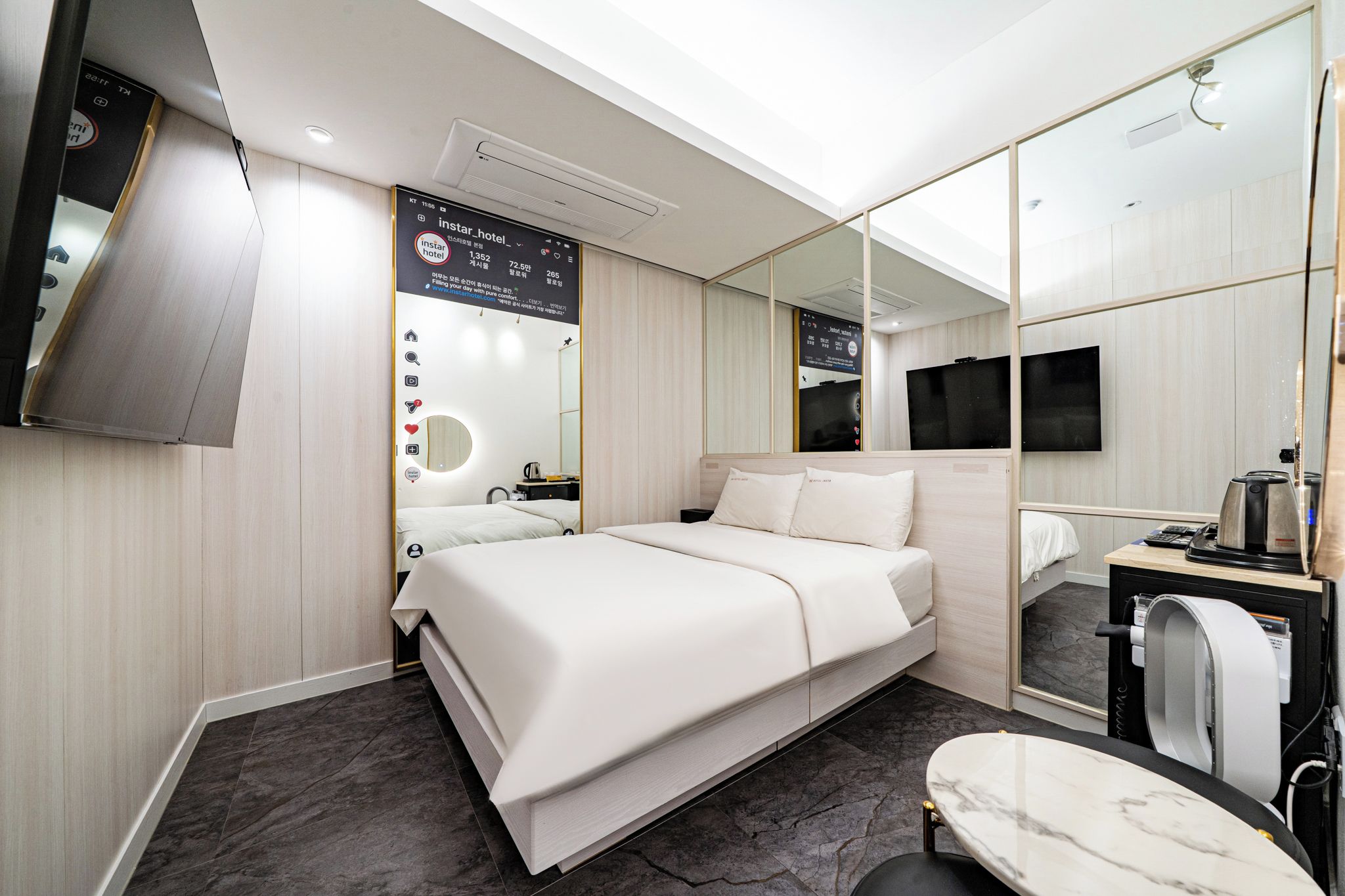 Et moderne hotelværelse med seng, et lille bord, et spejl, et fjernsyn og et panel monteret på væggen.