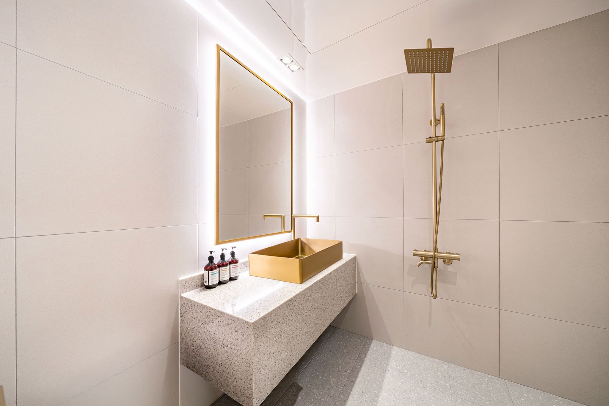 A modern bathroom with a freestanding gold sink, a large mirror, and a gold showerhead.