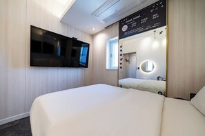 A hotel room with a large flat-screen TV mounted on the wall, a bed with white bedding, a large mirror with a round light, and a window providing natural light. - Insta Hotel - Main Branch (Suwon)