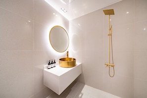 Une salle de bain moderne avec un meuble-lavabo blanc, un lavabo doré et une pomme de douche dorée.