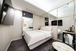 Una habitación de hotel moderna con cama, una mesita, un espejo, un televisor y un panel de control en la pared.