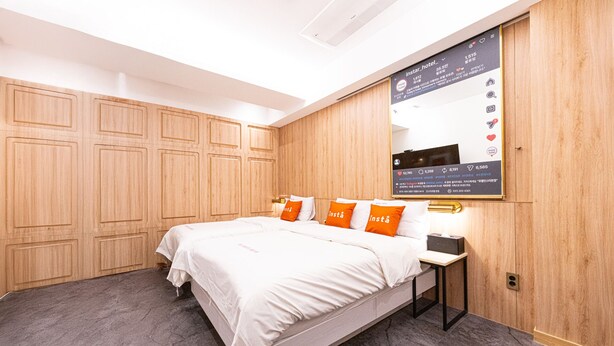 A hotel room with a bed, a bedside table, and a wall-mounted screen displaying hotel information. - Insta Hotel - Main Branch (Suwon)