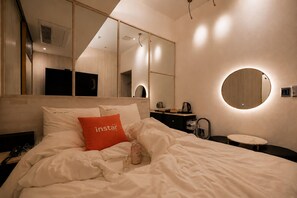 Una habitación de hotel con una cama, una mesita de noche, un espejo redondo, una pequeña mesa redonda y un tocador.