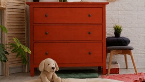 A red dresser with drawers, a small stool with a cushion, and a plush dog toy on a bed. - Insta Hotel - Main Branch (Suwon)