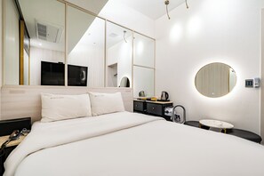 Habitación de hotel con cama, escritorio, espejo, espejo redondo, mesita y teléfono instalado en la pared.