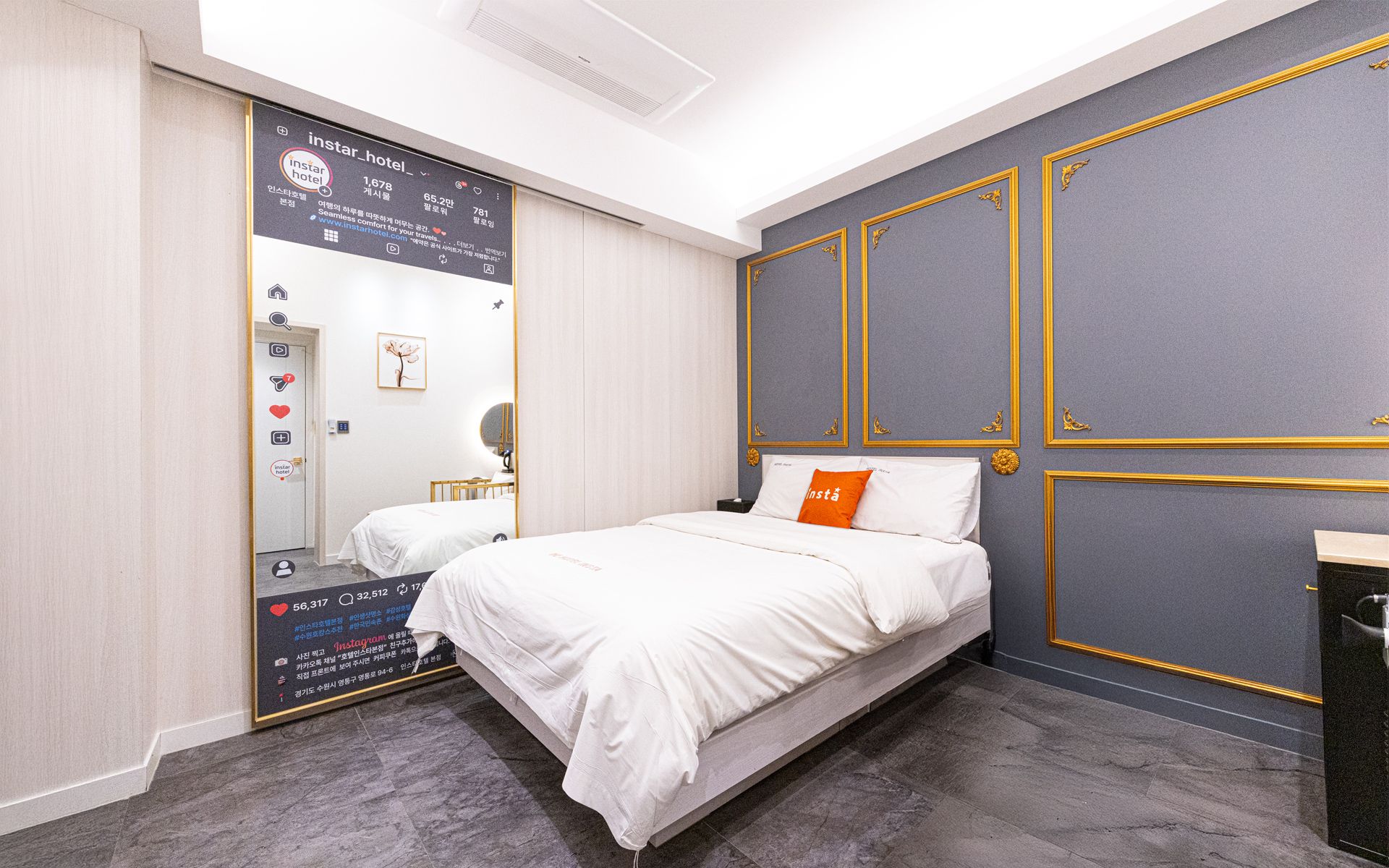 A modern hotel room with a large bed, a bedside table, a mirror, and a wardrobe with a digital display.