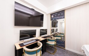 Ett hotellrum med en stor platt-TV, två datorskärmar, ett skrivbord med tangentbord och mus samt två stolar.