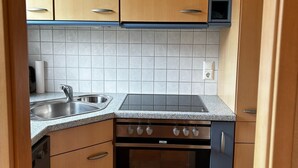 Cocina compacta con armarios de madera, pileta de acero inoxidable, horno integrado y una mesada con estufa.