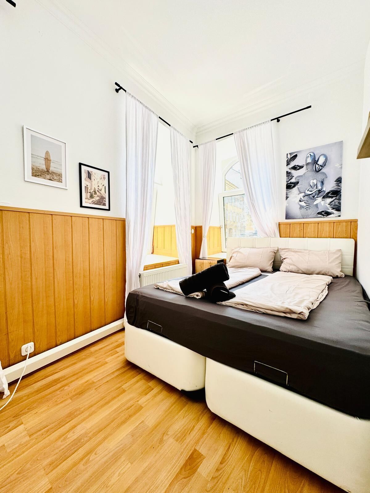 Un dormitorio con cama, paneles de madera, una ventana con cortinas y obras de arte en las paredes.