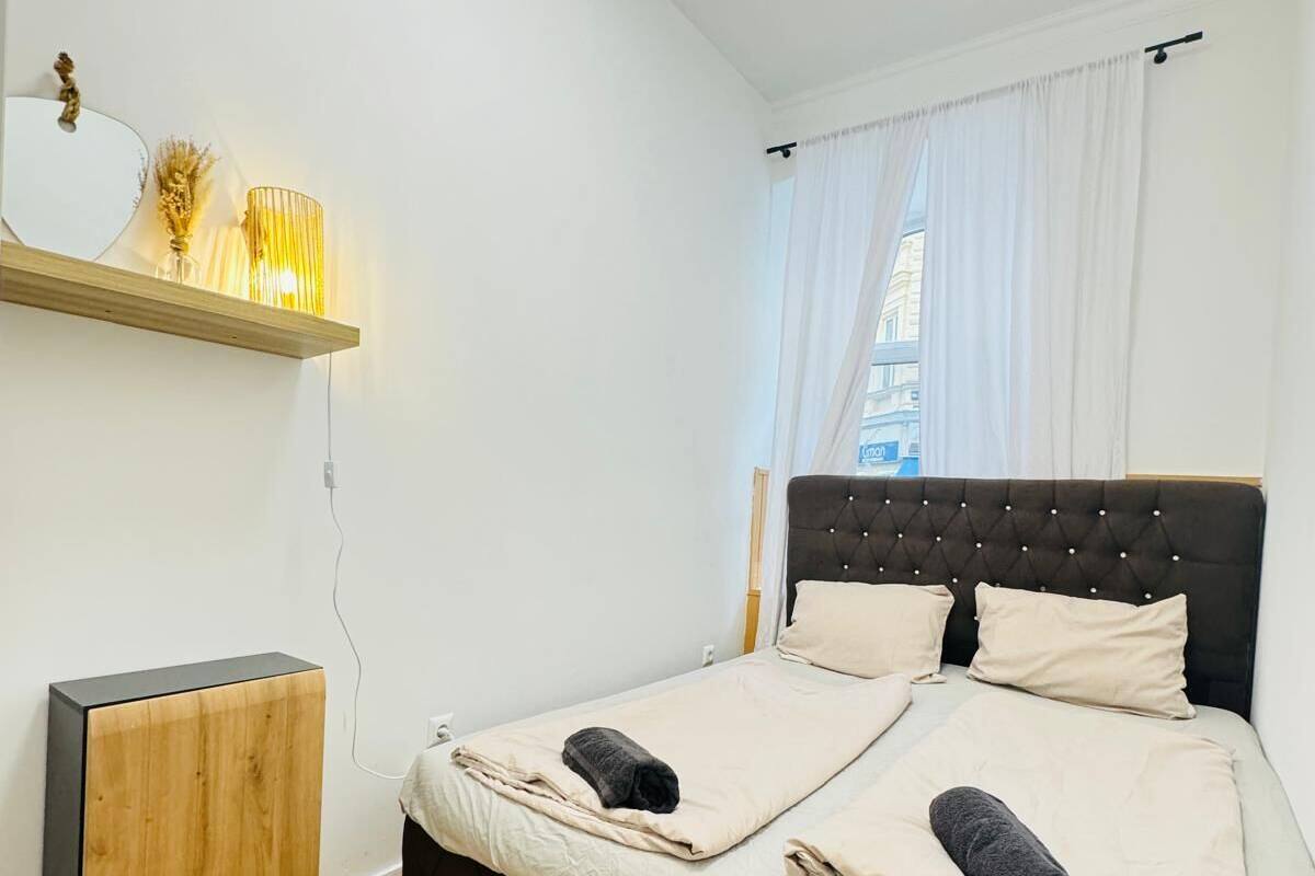 A bedroom with a bed, a bedside table, a mirror, and a shelf with a lamp.