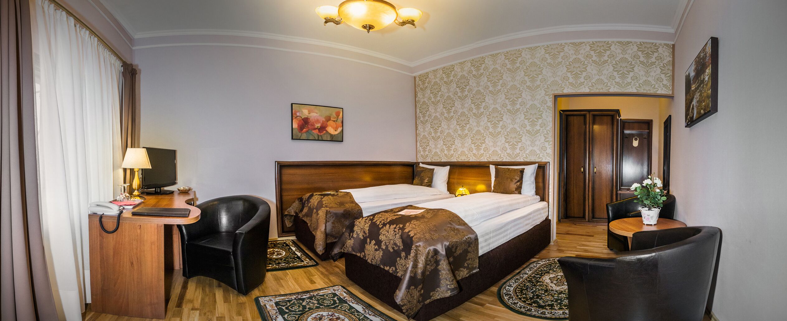 Ein Hotelzimmer mit einem großen Bett, einem Schreibtisch mit Lampe, einem Sessel, einem kleinen Tisch mit Vase und einer Tür zu einem weiteren Raum.