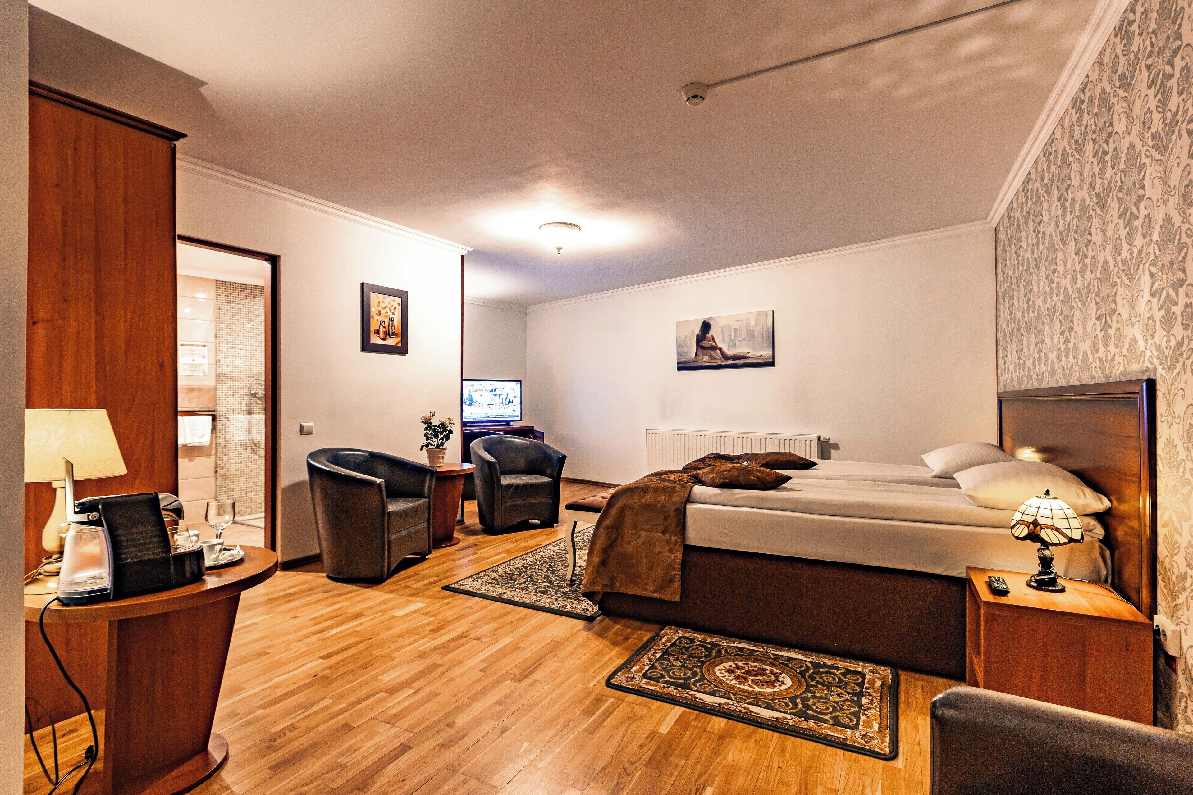 A hotel room with a bed, a desk, a chair, a TV, and a lamp.