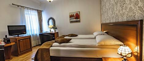 Ein Hotelzimmer mit Bett, Nachttisch, Lampe, Fernseher, Schreibtisch und einem Fenster mit Vorhängen.