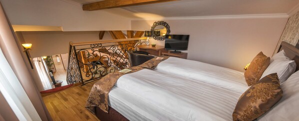 A bedroom with a large bed, a TV, a desk, and a staircase.
