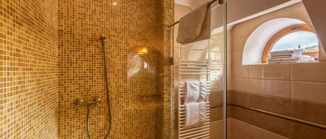 A bathroom with mosaic tile walls, a glass shower enclosure, and a towel rack with folded towels.